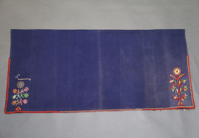 A hero shot featuring an indigo tubular skirt with intricate floral embroidery, adorned with pompoms, plastic sequins, and small brass coils with teardrop-shaped shell pendants