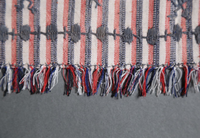 A detailed shot of the textile’s fringes in black, blue, red, and white threads