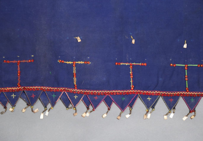 A close-up shot featuring the T-shaped embroidery motifs above the continuous triangular design at the bottom of the skirt, which is embellished with brass coils with shell pendants and cross-shaped embroideries