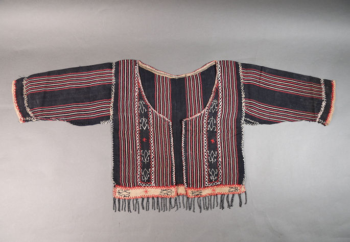 A feature shot of a female upper garment inspired by traditional Itneg or Tingguian designs. It showcases frog-like and lizard-like embroidery motifs in black and white, along with diamond, star-like, and zigzag motifs in red and white. Black beaded fringes embellish the bottom of the garment