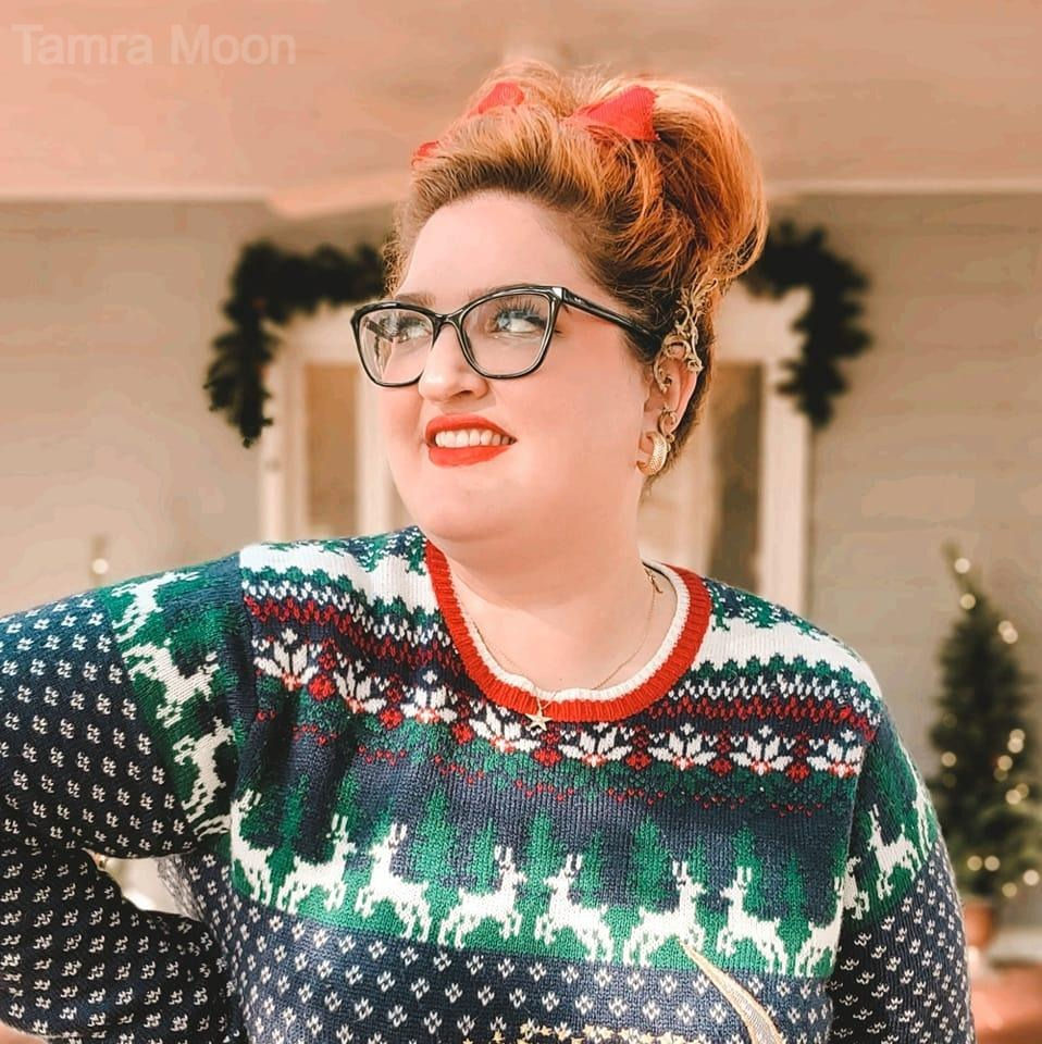 Tamra Moon, a plus size content creator, wearing a cute Christmas sweater and a red bow in her hair.