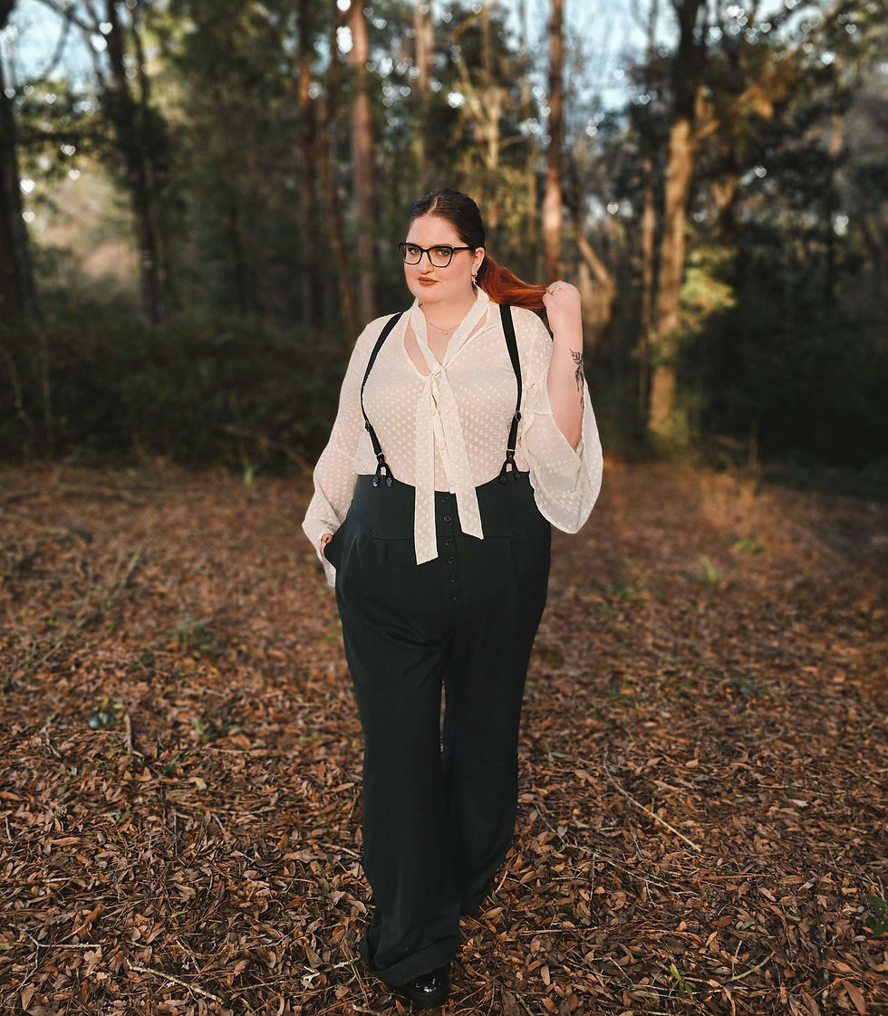 Tamra Moon wearing a 1940's inspired outfit of high-waisted green wool trousers, black suspenders, and a sheer blouse with flowy sleeves.