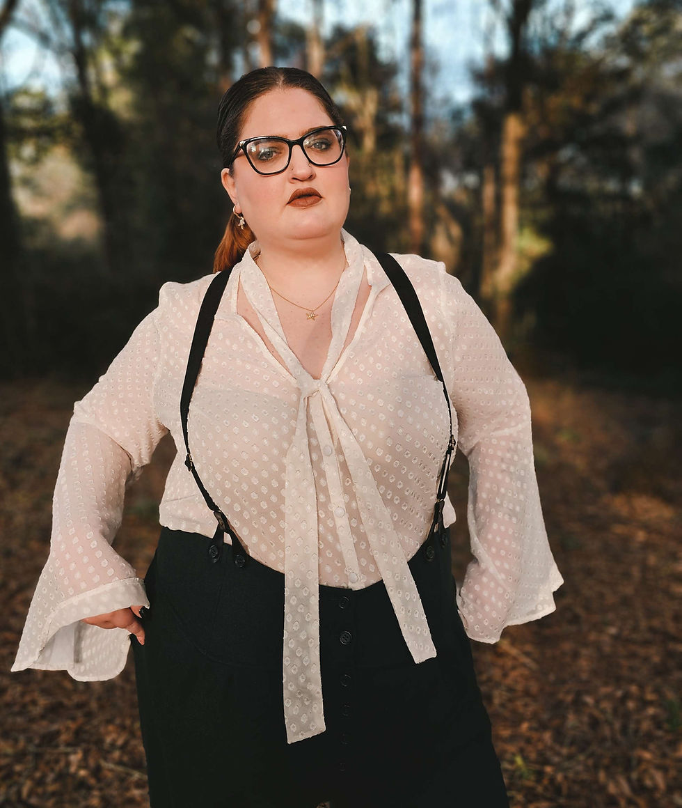 Tamra Moon wearing a 1940's inspired outfit of high-waisted green wool trousers, black suspenders, and a sheer blouse with flowy sleeves.