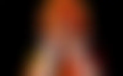Isabelle Drummond caracterizada como Emília, com peruca laranja e amarela, figurino vermelho e amarelo e luvas brancas.