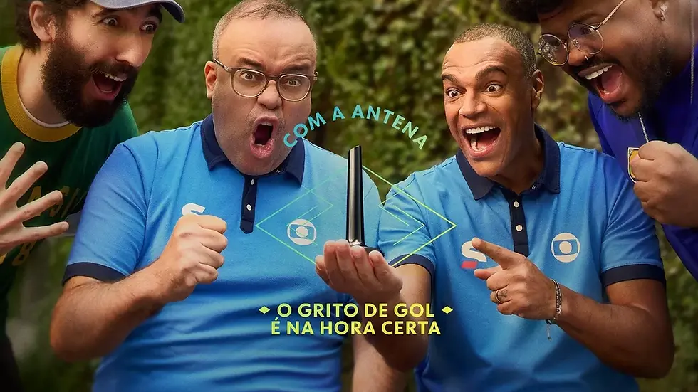 Apresentadores da Globo e torcedores comemoram ao lado de uma antena digital em campanha sobre transmissão sem delay na Copa.