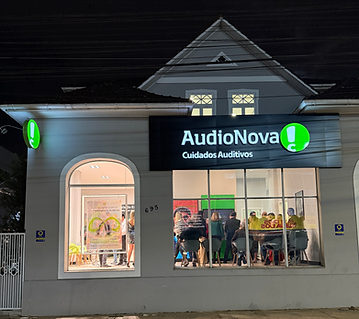 Fachada da AudioNova Cuidados Auditivos iluminada à noite.