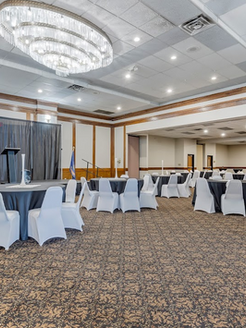 Spacious ballroom with round tables, chairs, and a stage