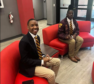 Two Kappa League men in ties sitting on red couches, one smiling