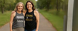 Two smiling women in empowering gym shirts: one wearing "Progress is the New Perfection" in gray and the other wearing "Strong is Ageless" in black — strength and support in midlife fitness fashion.
