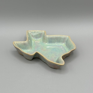 A ceramic dish shaped like Texas with a light, pastel blue and green glaze.