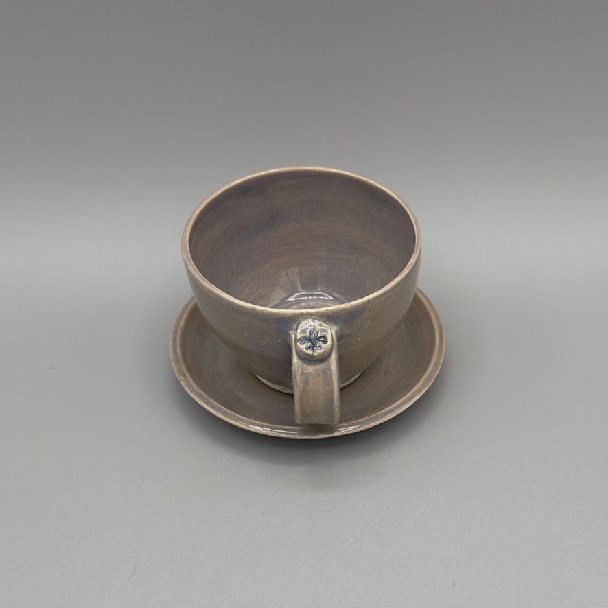Handcrafted gray opal ceramic tea cup and saucer set with floral handle detail.
