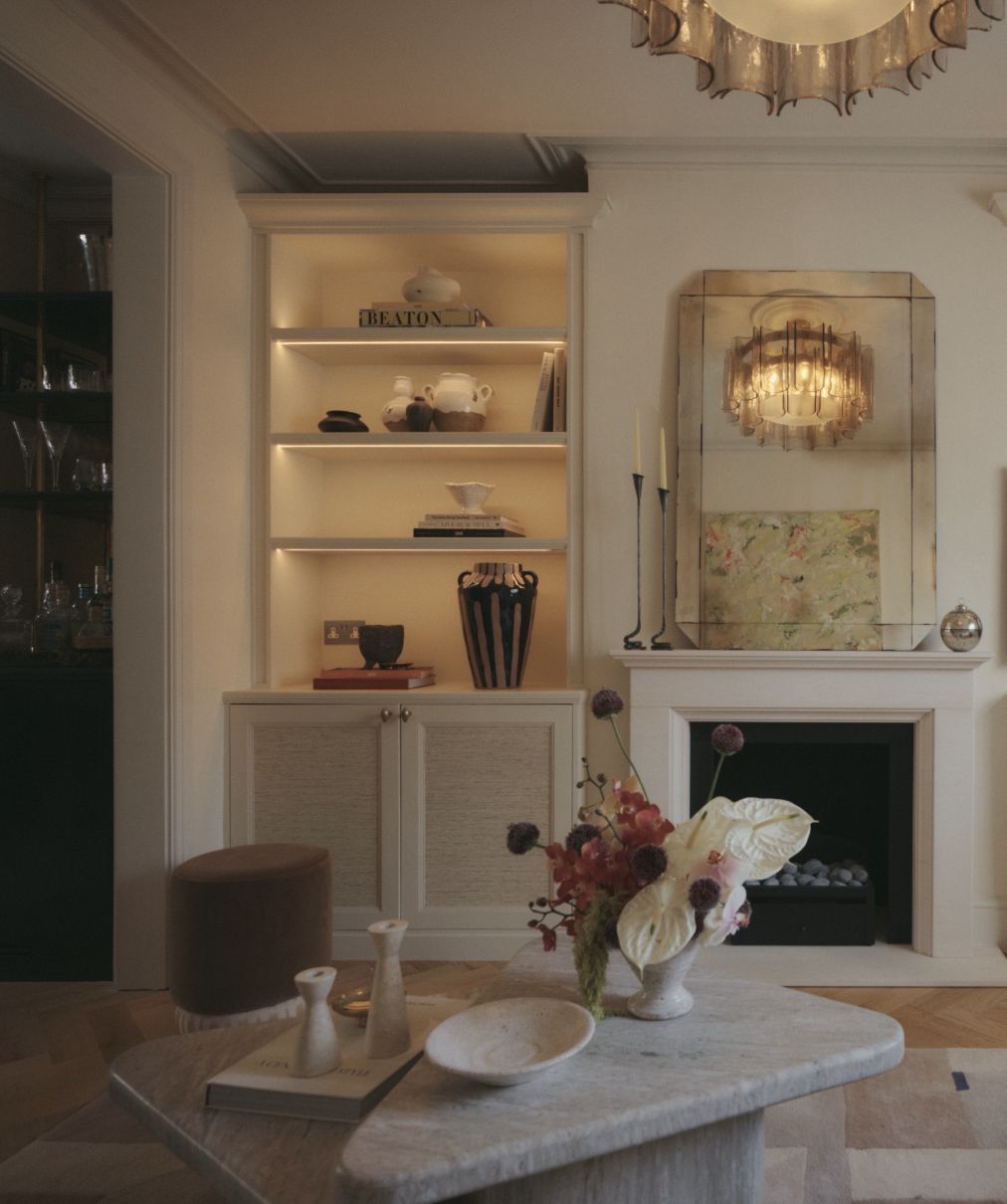 Chiswick House living room with lit alcove shelving, a stone fireplace and a smoked-glass ceiling light