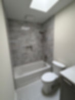 Modern bathroom with grey tile shower, tub, and skylight.