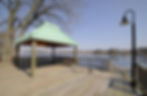 Wooden deck with a green-roofed gazebo overlooking a lake.