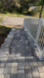 Stone paver steps with a white metal railing leading down.