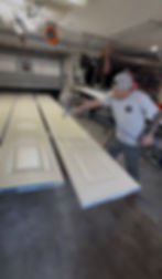 Worker spray painting white interior doors in a workshop.