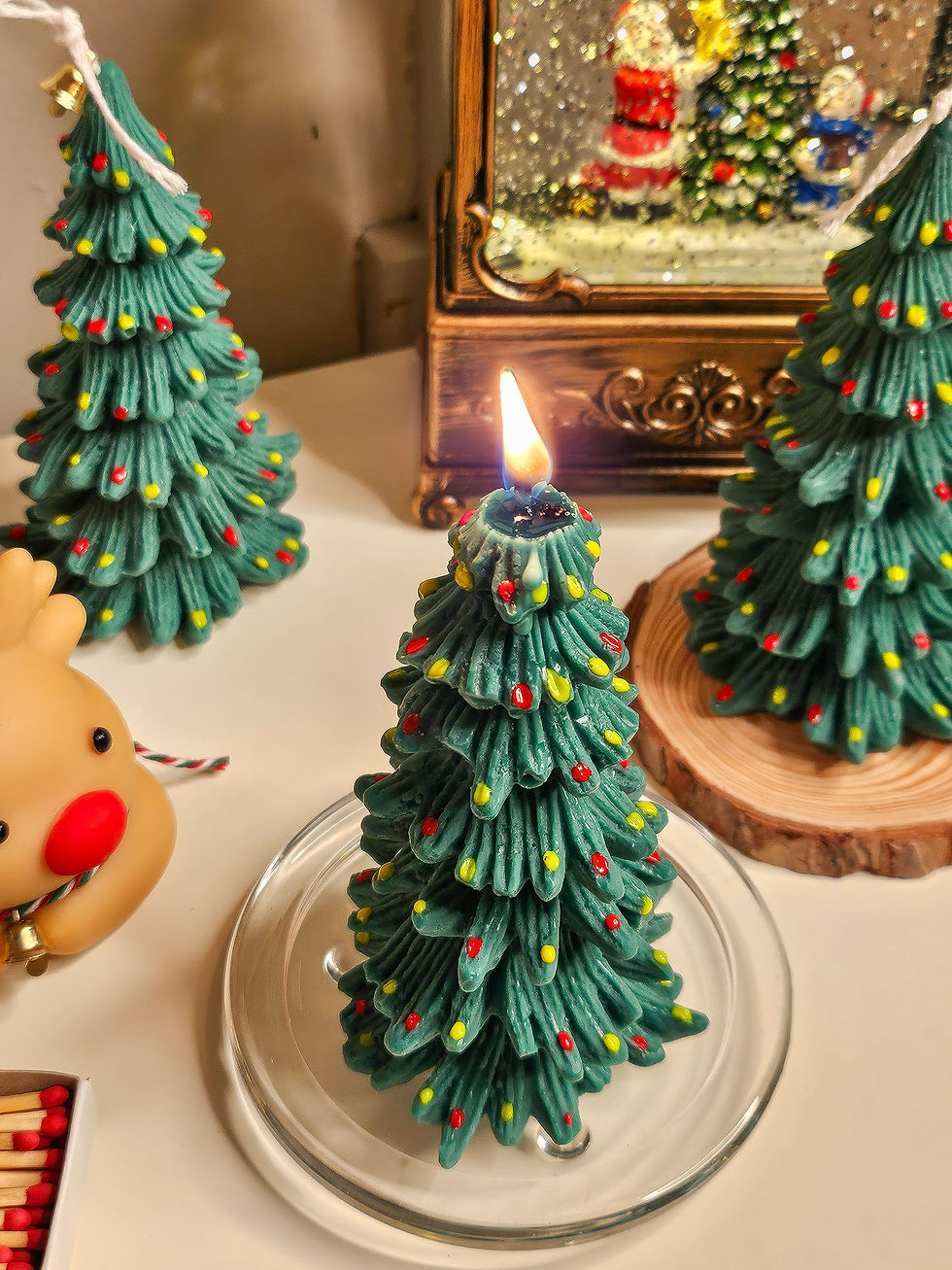 Christmas tree candle lit beside a reindeer candle on a glass plate, creating a warm holiday glow.