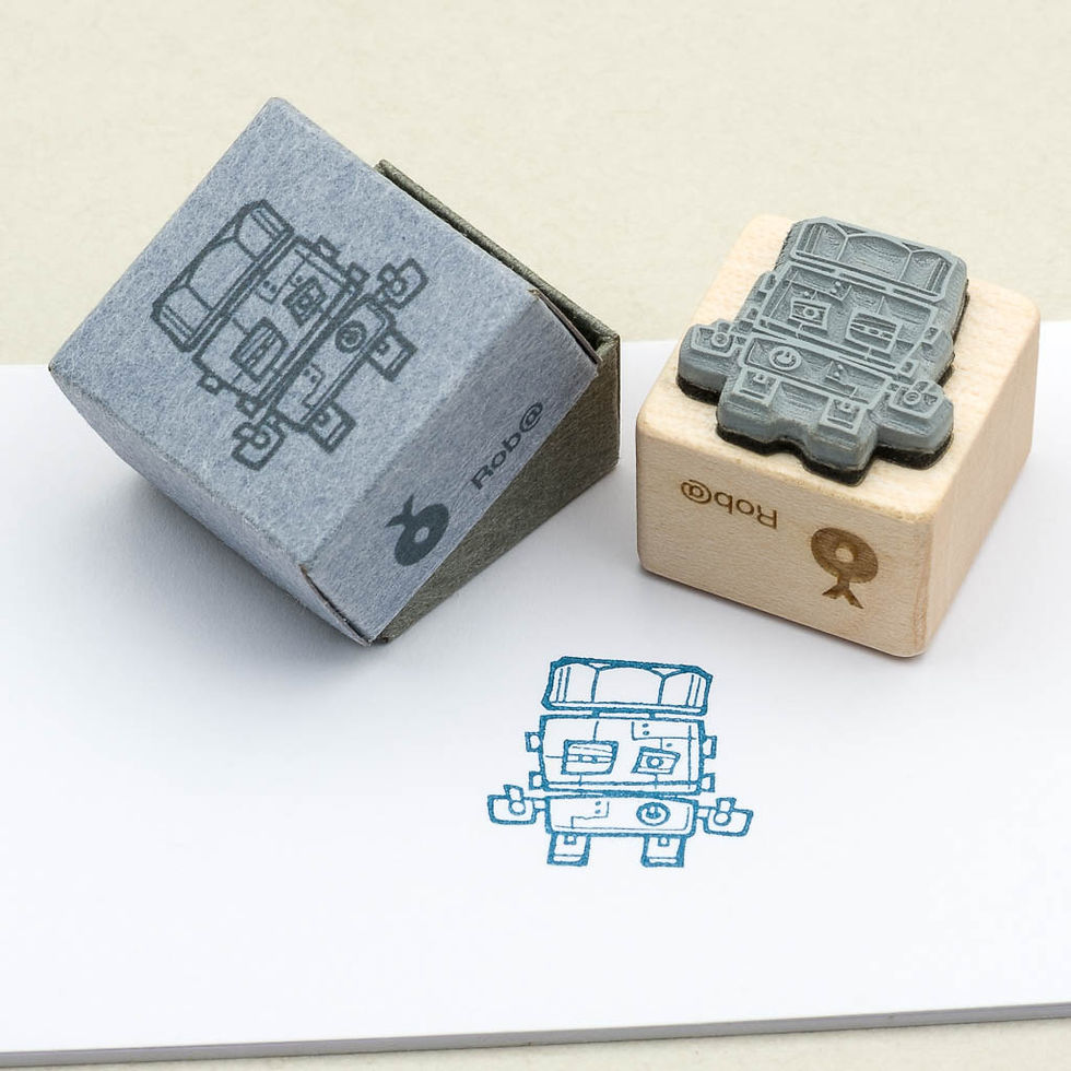 Roboter-Stempel aus Holz, auf weißem Papier blau gestempelt. Passende Aufbewahrungs-Box aus Papier. Ansicht Stempelseite.