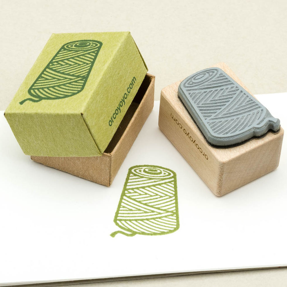 Motivstempel einer Garnkone mit Ahornholgriff und grün- und sandfarbener Kartonschachtel, Ansicht der Stempelseite.