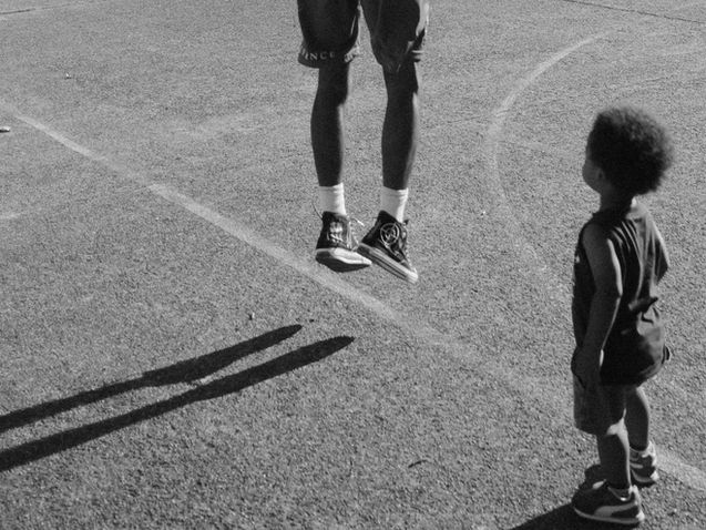 Black and white photo of basketball player shooting a basket with young child looking