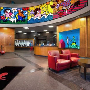 Bright St. Jude Children's Research Hospital lobby with colorful cartoon art, red chairs, blue sofa, and red luggage carts near the front desk.