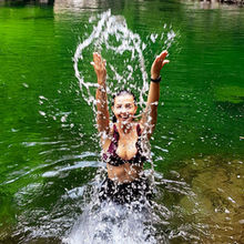 Mujer lanza agua con las manos mientras disfruta en un pozo de agua natural en la selva colombiana