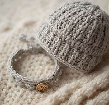 Gray knitted baby hat and bracelet on a soft blanket background.
