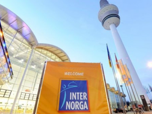 Welcome banner for Internorga event at illuminated glass building, flags, and tower against a blue sky. Text on banner reads "Welcome."