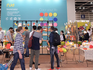 People browsing colorful products at a vibrant trade fair booth with a blue wall displaying "Recycled Leather" and "Color your life."