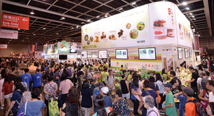 Crowded trade show with people browsing booths. Large white signs and screens display food items. Red "Exit Only" sign above. Busy atmosphere.