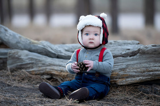 Little boy with a plaid winter hat on in front of a log
