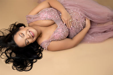 pregnant woman laying on her side cradling her belly and smiling in pink gown