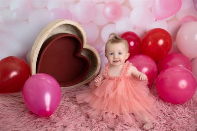 Photo of a little girl dressed in pink surrounded by pink balloons and hearts