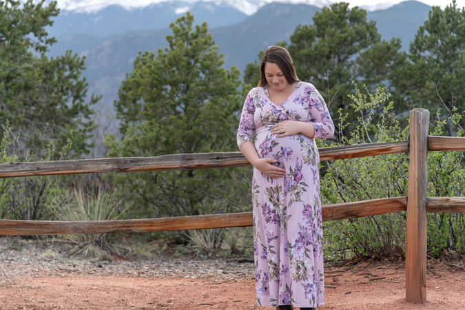 Spring maternity photo in lavender floral dress against mountain backdrop
