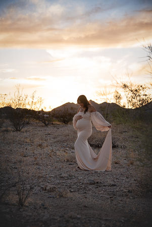 pregnant woman poses at sunset against the mountains in a white maternity gown