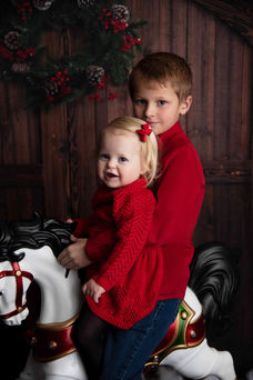 Photo of a brother and sister dressed in red on an antique christmas rocking horse