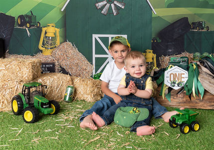 Photo of two brothers surrounded by green tractors and a green barn