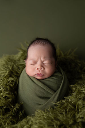 Newborn wrapped in forest green fabric sleeps all bundled up