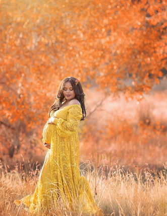 autumn maternity photo in yellow gown against orange leaf backdrop