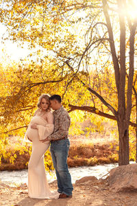 fall maternity photo in beige gown against yellow leaf backdrop