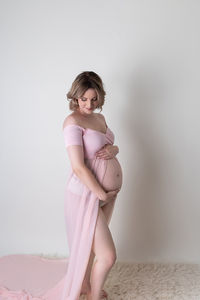 pregnant woman poses in open front light pink gown