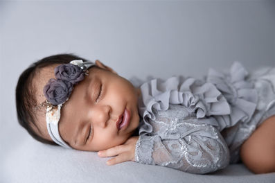 newborn baby girl in grey ruffled outfit with floral headband sleeps on stomach