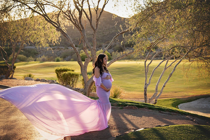 pregnant woman in light purple gown poses at sunset on a golf course