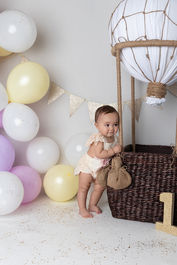 Photo of a little girl with yellow, pink, and white balloons and a little hot air balloon