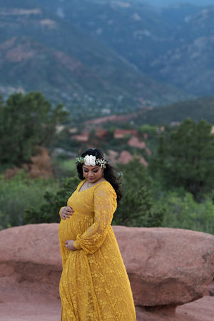 pregnant woman in yellow lace gown and flower crown poses against mountain backdrop