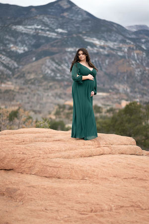 maternity photo in dark green gown against snowy mountains