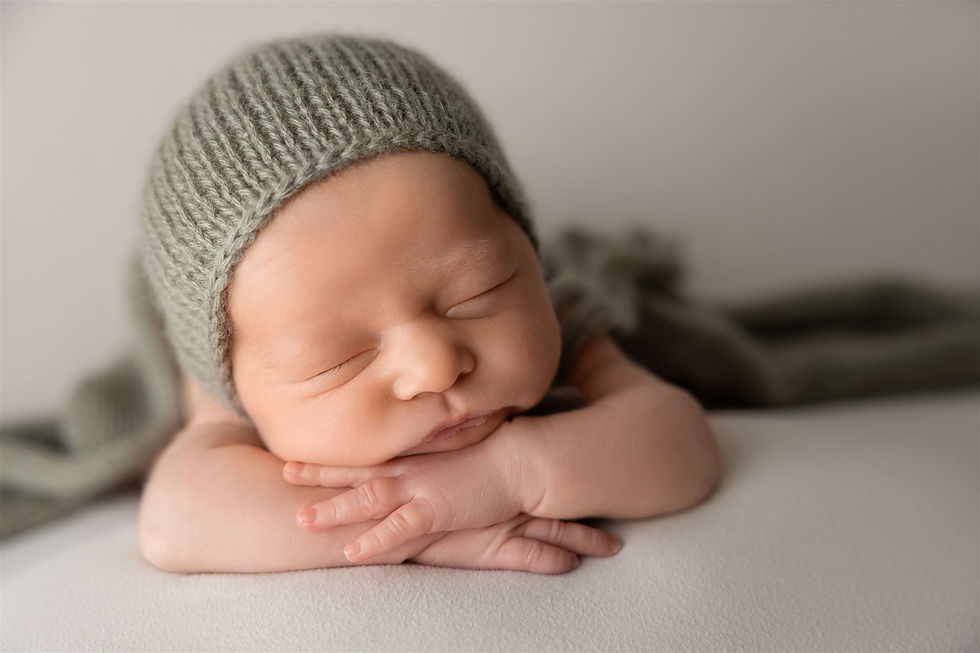 newborn baby wearing green knit hat sleeps resting chin on hands