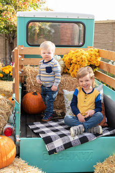 Photo of two brothers in the back of an old teal pickup truck with hay and pumpkins