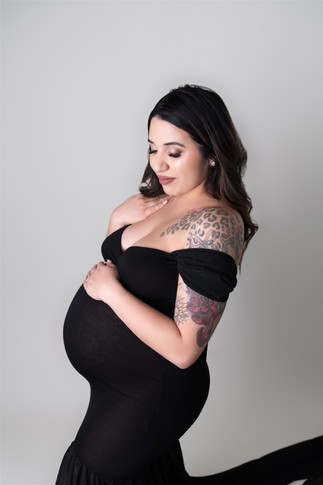 pregnant woman in black gown looking down and cradling belly 