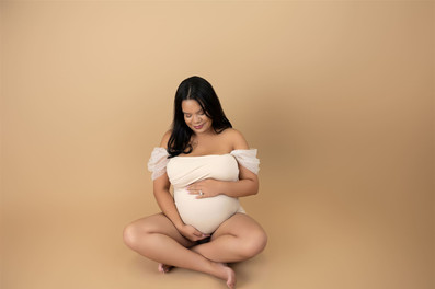 pregnant woman wearing off-white maternity leotard sitting cross legged on the ground